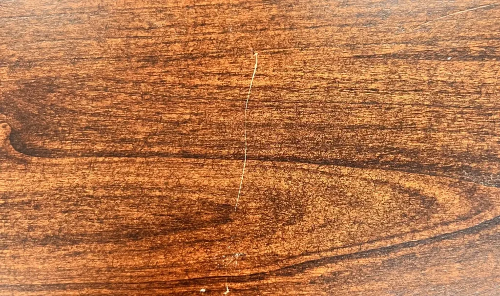 Fine scratch through the finish on a stained hardwood furniture surface.