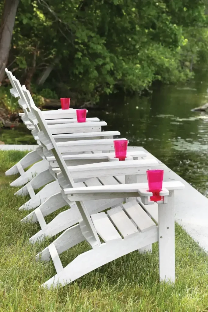 Berlin Gardens standard poly accessories, a row of white poly Adirondack chairs with cupholders lined up on a lawn.