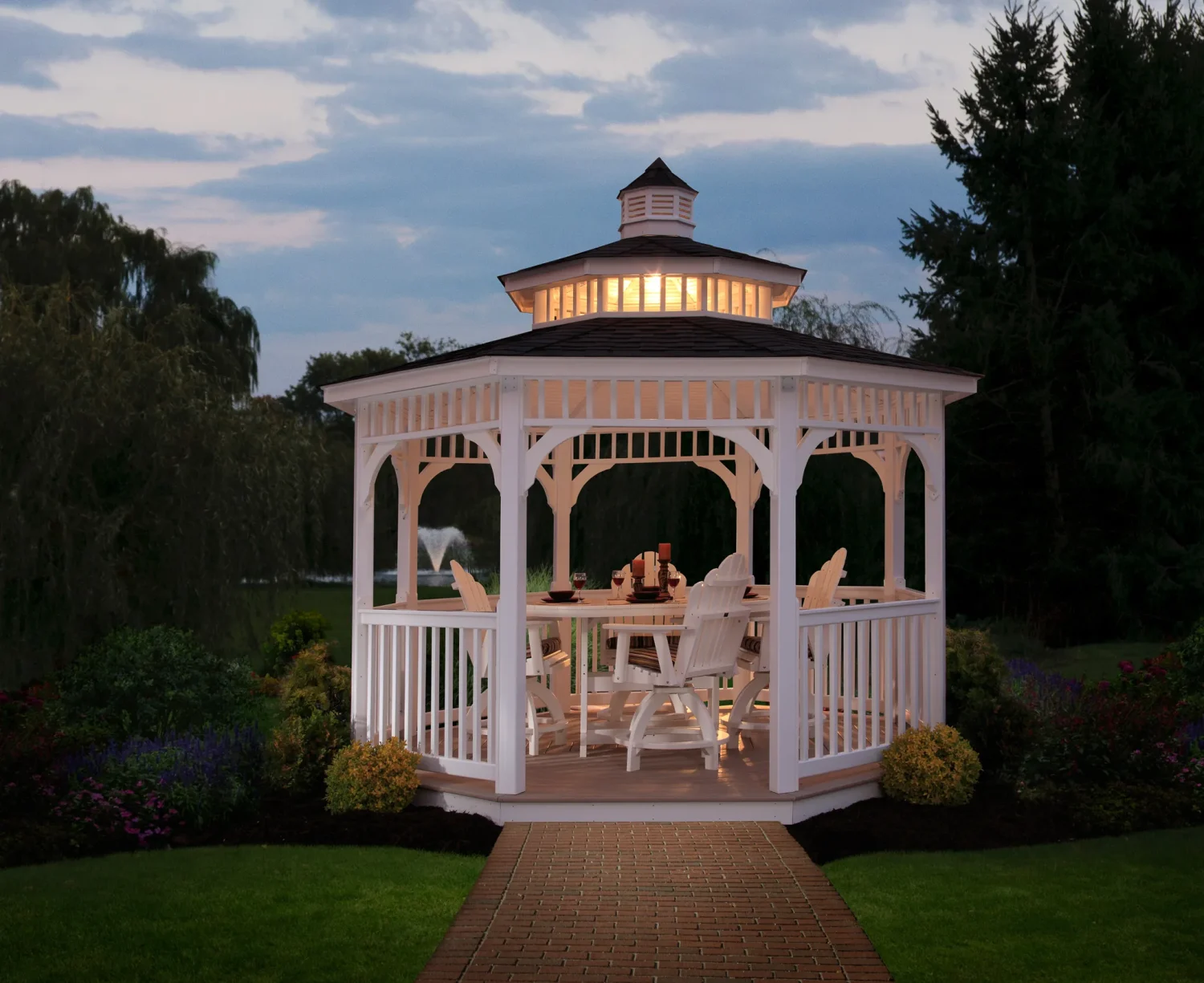 Berlin Gardens gazebos collection, a white octagonal gazebo with a cupola and railings lit at dusk in a landscaped yard.