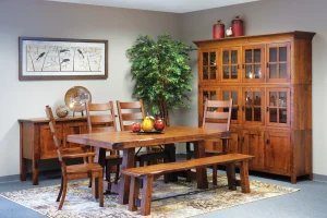 Amish Sadler Mission dining collection in rustic cherry, shown with a trestle table, bench, chairs, and a large hutch.